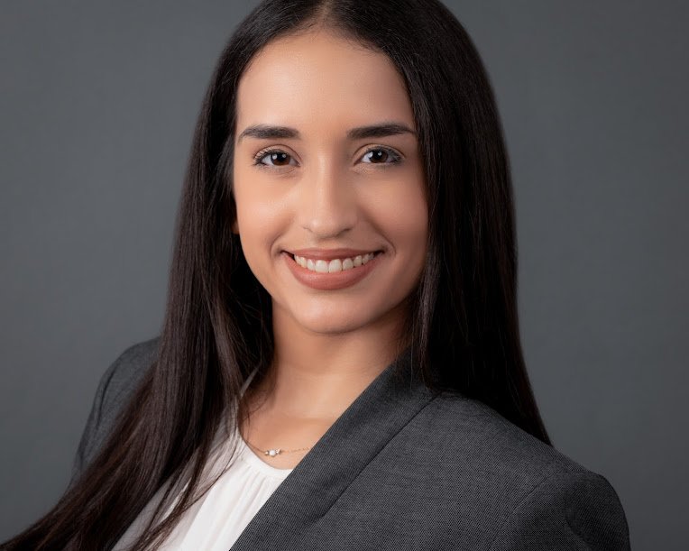 Professional headshot — woman in gray blazer, dark background